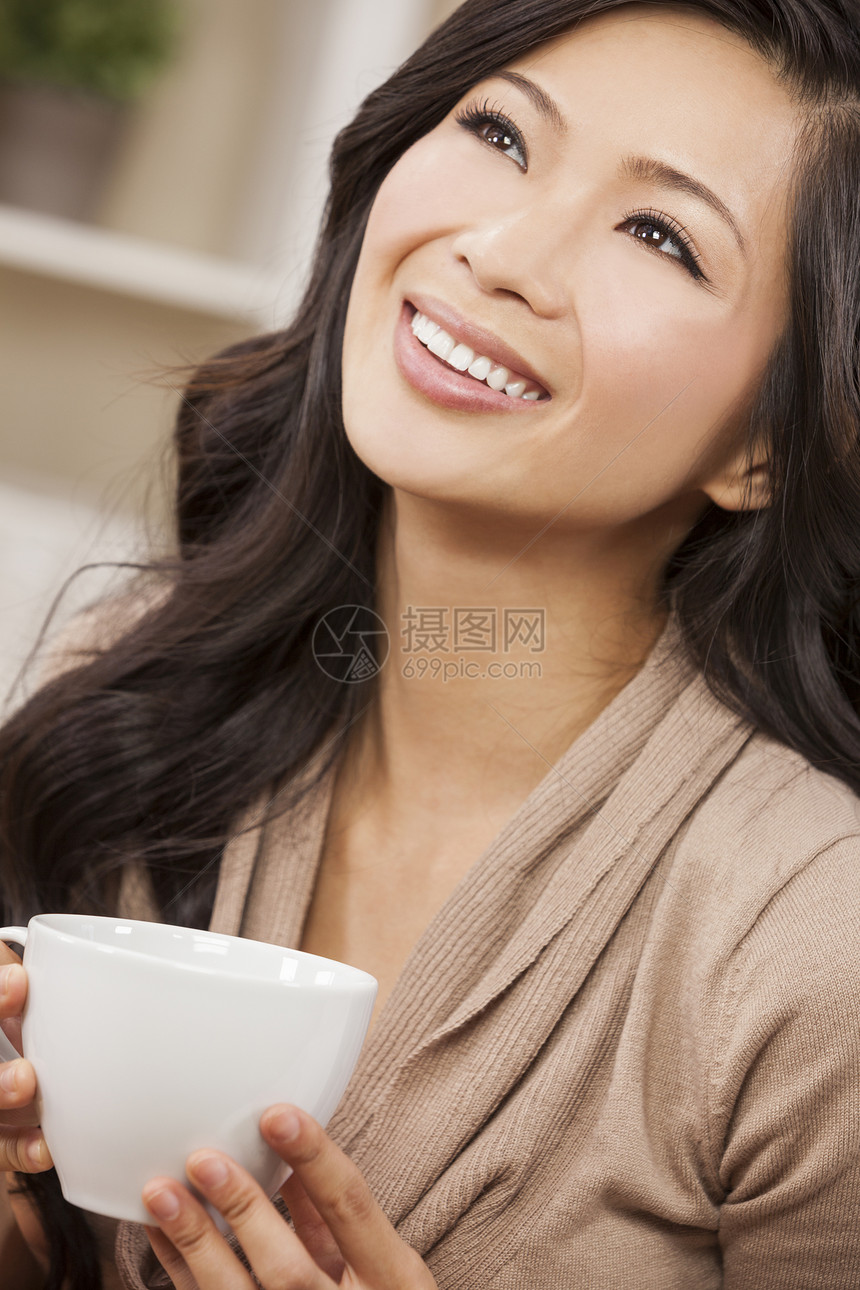 个美丽的轻的中国亚洲东方女人,带着种美妙的牙齿微笑,白色的杯子里喝茶喝咖啡图片
