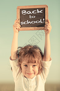 快乐微笑的小学生着小黑板,带着课文回学校天空的背景下背景图片