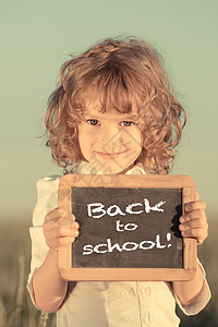 快乐微笑的小学生着小黑板,带着课文回学校天空的背景下背景图片