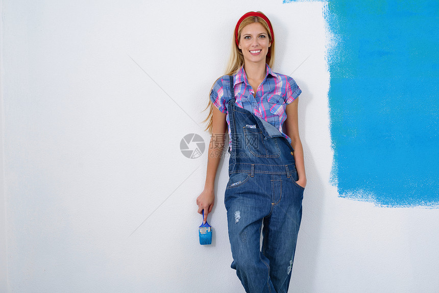 快乐微笑的女人用蓝色绿色的新房子画内墙白色的墙图片