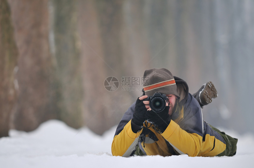 职业摄影师穿着黄色夹克躺雪地上拍摄图片