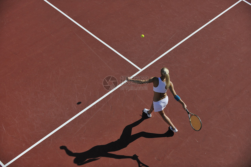 轻健康的女人大早就橙色的网球场上户外打网球图片