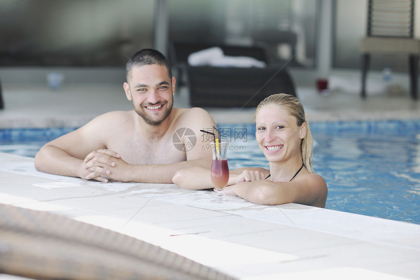 快乐的轻夫妇室内健康游泳池享受快乐的放松喝鸡尾酒图片