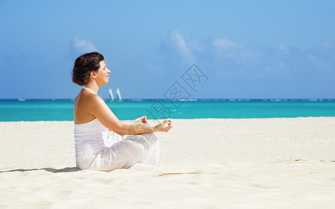 海滩上坐着莲花姿势的快乐女人的冥想图片