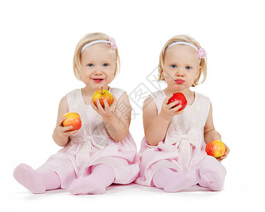 孩子,食物双胞胎的两个相同的双胞胎女孩玩苹果背景图片