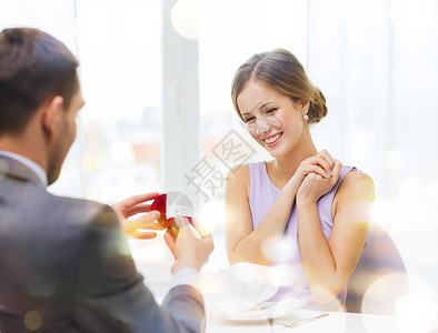 兴奋的年轻女人看着男朋友与订婚戒指餐厅图片