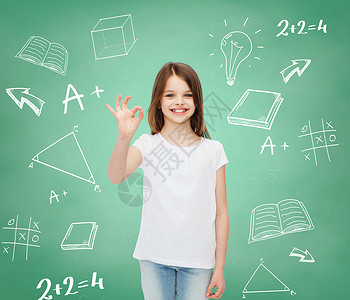 广告,学校,教育,童人微笑的小女孩穿着白色T恤,带涂鸦背景的绿板上OK标志图片