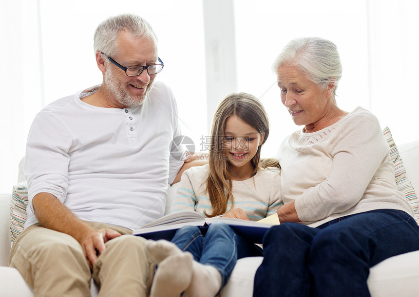 家庭,世代人的微笑的祖父,孙女祖母坐家里的沙发上看书图片