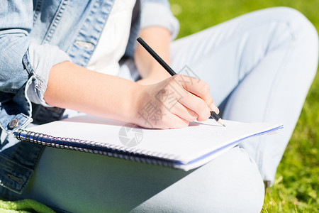 生活方式,暑假,教育人的特写轻女孩用铅笔写字笔记本,坐公园的草地上图片