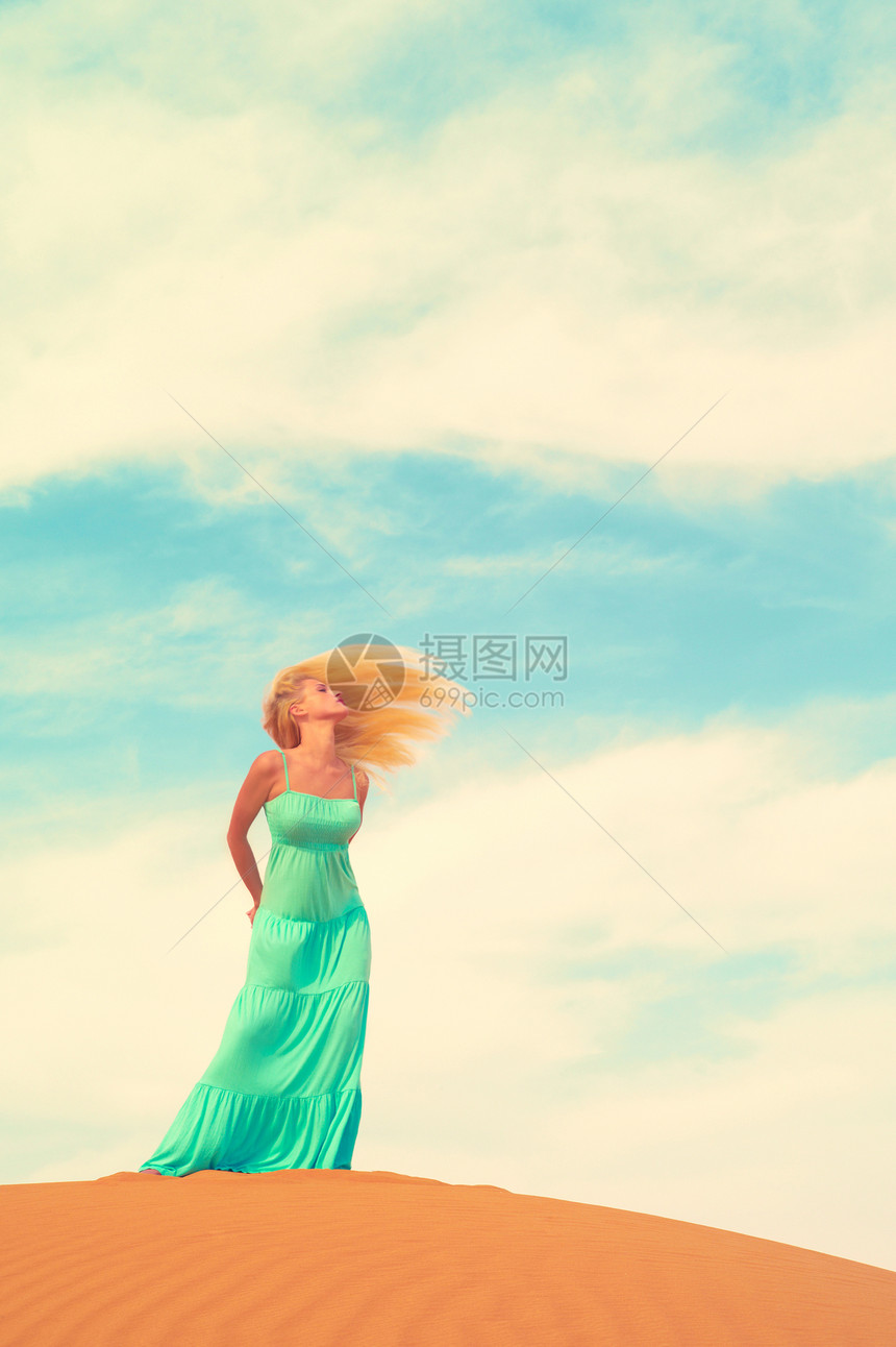 美丽的金发女郎穿着蓝色的连衣裙,穿着橙色的沙漠阿联酋图片