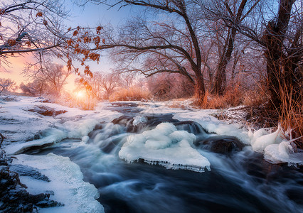 日落时令人惊叹的河流的冬季森林冬天的风景雪树,冰,美丽的冰冻河流,雪丛,黄昏中五颜六色的天空模糊的水小瀑布水背景图片