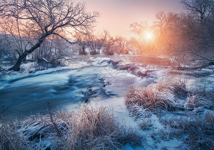 日落时令人惊叹的河流的冬季森林冬天的风景雪树,冰,美丽的冰冻河流,雪丛,黄昏中五颜六色的天空模糊的水小瀑布水背景图片