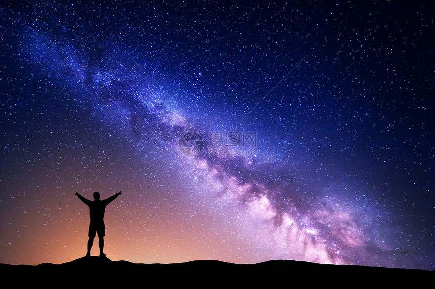 紫色的银河,个站着的人的轮廓,举手臂山上美丽的星系的夜景宇宙夜空中银河黄光图片