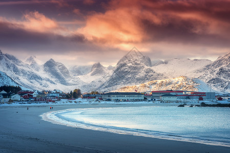美丽的北极沙滩,冬季挪威洛福滕群岛日落时蓝色的大海风景雪山,天空橙色的云,水,村庄建筑,步行的人自然背景图片