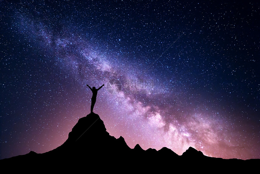 充满活力的银河景观五颜六色的夜空,星星个站立的运动女孩的轮廓,美丽的星系的背景上的山峰上举手臂图片
