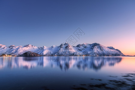 美丽的雪覆盖着群山,五彩缤纷的天空夜晚反射水中冬季景观海洋,雪岩,蓝天,倒影,日落时的阳光黄昏时分,挪威的洛芬岛背景图片