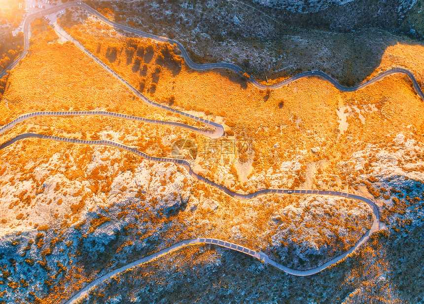 空中观看山曲线道路与汽车,橙色森林日落欧洲秋季景观与沥青道路,树木岩石上穿过公园的高速公路飞行无人机的顶部视图图片