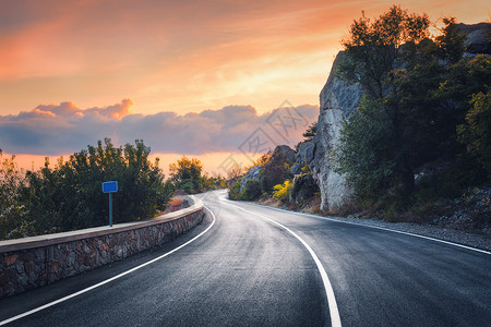日落时的山路风景与岩石,橙色阳光明媚的天空与云美丽的沥青路晚上的夏天复古色调旅行背景高速公路的风景运输背景图片