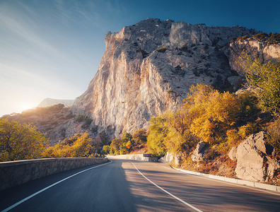 日落时的山路美丽的天空五颜六色的景观,高岩石,蜿蜒的沥青路,橙色的叶子,蓝色的天空,秋天的云旅行山中巷道的风景背景图片