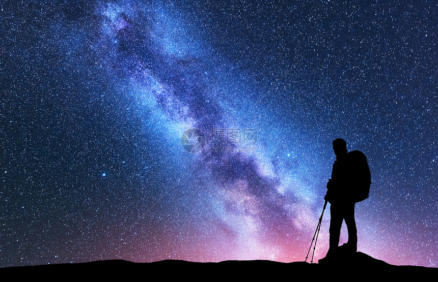 夜晚,带着背包徒步旅行杆的男人令人惊叹的紫色银河上的剪影风景与人,明亮的银河,天空与星星美丽的星系旅行图片