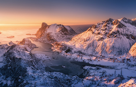 挪威洛福滕群岛日落时美丽峡湾的鸟瞰图冬天的风景雪山,蓝色的大海橙色的天空太阳雪路村庄中岩石的顶部景观北部海背景图片