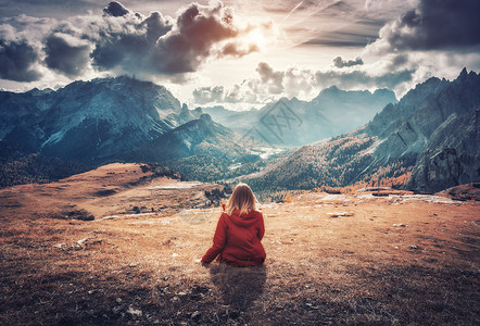 轻的女人坐田野上,意大利白云石的秋天日落时,着雄伟的山脉风景与女孩,多云的天空,橙色的草,高岩石与森林秋天意大背景图片