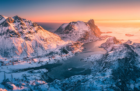 挪威洛福滕群岛日落时美丽峡湾的鸟瞰图冬天的风景雪山,蔚蓝的大海金色的阳光雪中岩石的顶部景观,村庄北部海岸线背景图片