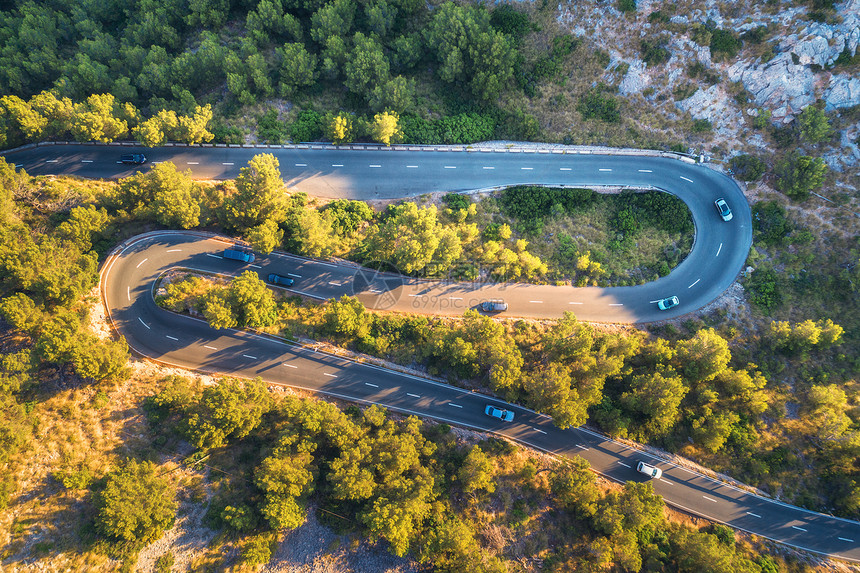 空中观看山曲线道路与汽车,绿色森林日落欧洲夏季景观与沥青道路,树木岩石上穿过公园的巷道飞行无人机的顶部视图图片
