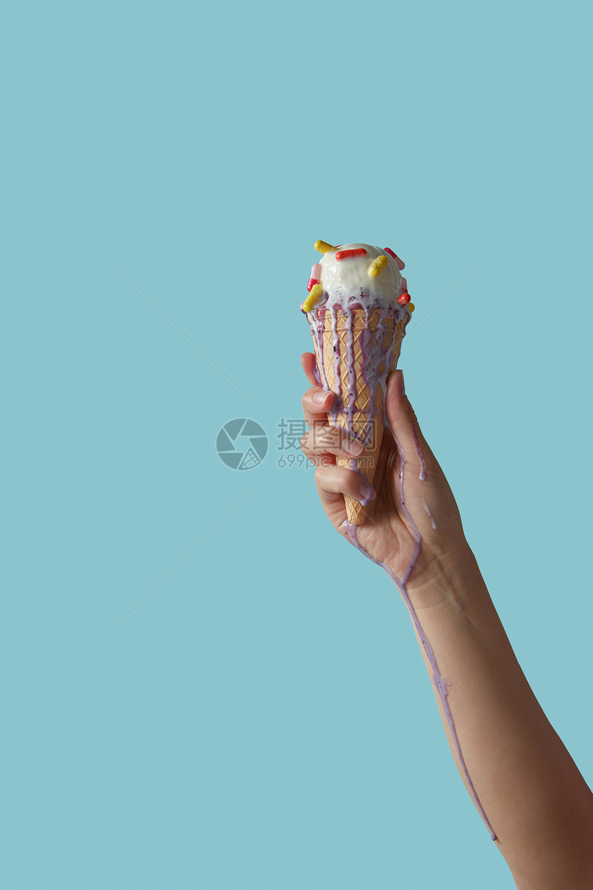 个女孩的手着个脆脆的华夫饼锥,融化的冰淇淋,彩色的药丸,雪糕溅她的手上,围绕着蓝色的背景,文字的图片