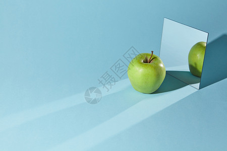 镜子里的表镜子里块绿色的苹果苹果的影子的倒影角线长的阴影来自苹果镜子蓝色的桌子表苹果绿色的,蓝色背景上的方形镜子,苹果背景