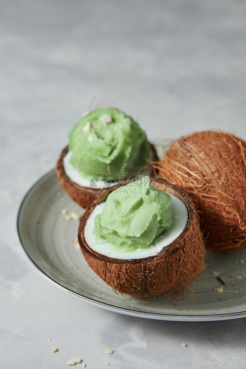 自制的绿色冰淇淋椰子壳上,整个椰子灰色的混凝土背景上,放置文字夏季甜点美味的新鲜绿色水果冰淇淋椰子皮与整个新鲜椰子图片