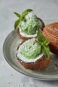 椰子与绿色冷冻薄荷甜点,绿色薄荷个盘子上的灰色背景素食的夏季食品美味的自制薄荷冰淇淋,个椰子壳上,个灰色的背景图片