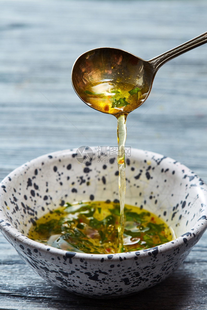 刚准备好的沙拉酱勺子里掉进陶瓷碗里,灰色的木制背景上放着橄榄油切碎的草药盐胡椒醋用橄榄油醋蔬菜香料自制的沙拉图片
