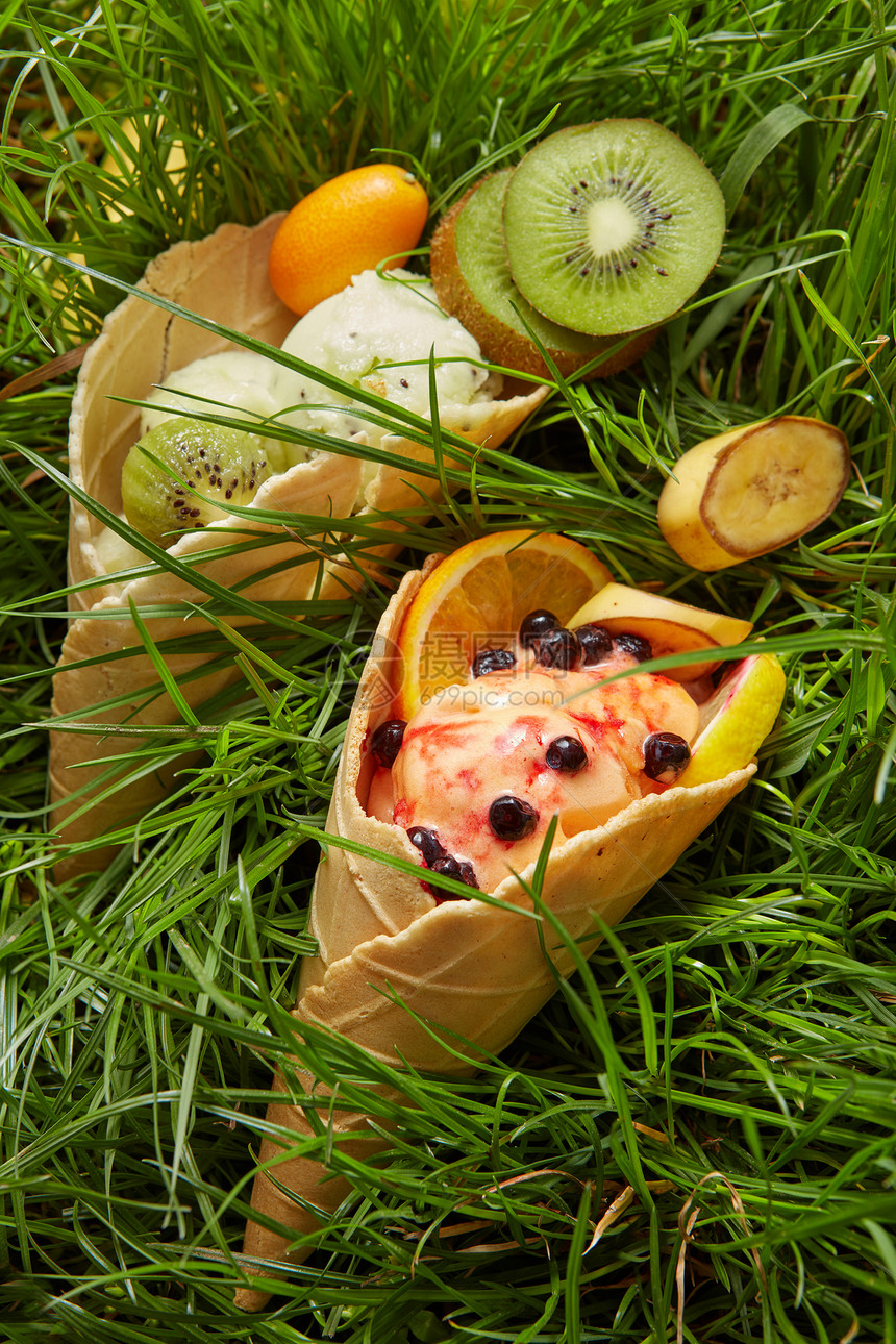 各种冰淇淋华夫饼锥与浆果新鲜水果香蕉,猕猴桃,橙色的背景上的绿色草华夫饼锥里的浆果冰淇淋图片