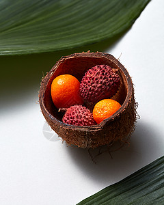 热带异国水果莱奇金橘椰子壳与常青叶分离白色背景特写照片椰壳中Lytchi金橘果实的特写,白色背景上分离出热带绿叶背景图片
