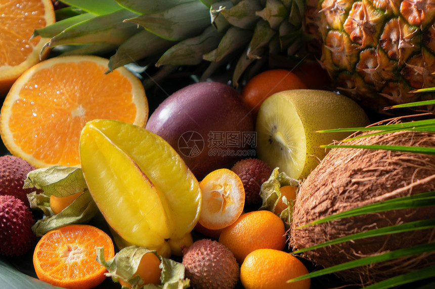 热带异国水果的分类半的橘子,荔枝,杨桃,菠萝,柠檬,physalis,椰子,荔枝与棕榈叶新鲜的外来机水果自然背图片