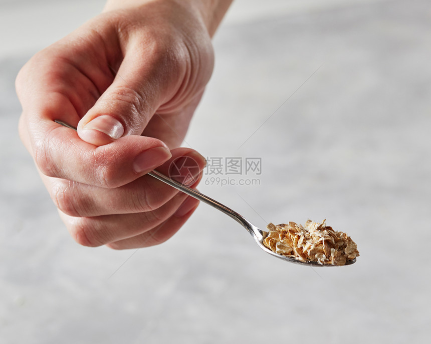 女孩手里着把勺子,灰色厨房桌子的背景上燕麦片健康饮食的女人手中勺生燕麦片灰色桌子的背景图片
