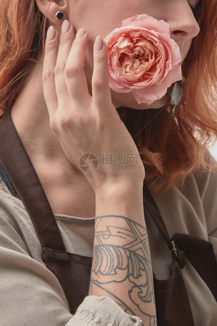 个红头发的轻女孩嘴里朵精致的粉红色玫瑰,纹身假日卡的纹身的红发女孩嘴里衔着朵粉红色的玫瑰明图片