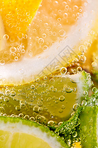 夏季装上市熟透的柠檬片石灰片放装水气泡的杯子里夏季饮料的观照片柠檬石灰的柑橘类水果,杯水中气泡夏季清爽鸡尾酒背景