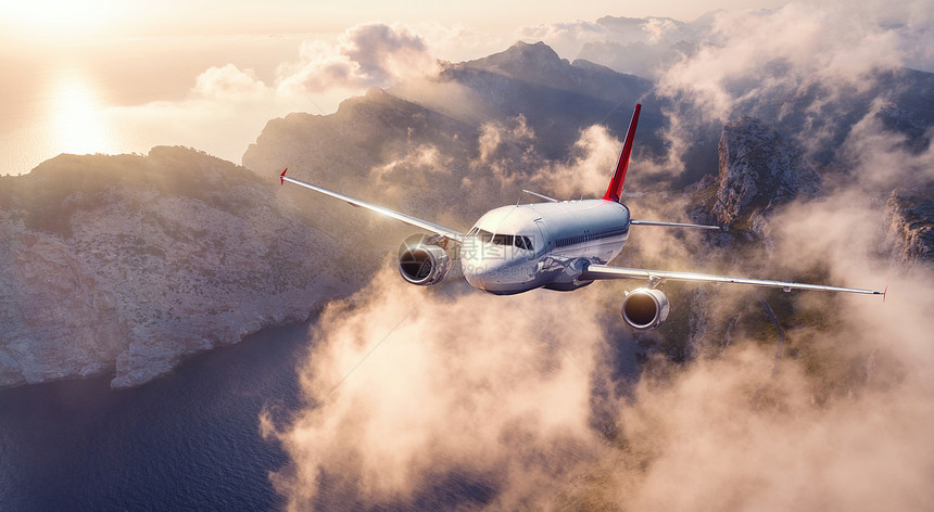 飞机夏天日落时飞过群山低云景观与客机,天空云,岩石,海洋,阳光商务旅行商业飞机飞机的鸟瞰图图片