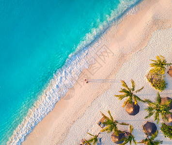 日落时,印度洋的沙滩上俯瞰雨伞棕榈树非洲桑给巴尔的夏天热带景观棕榈树阳伞步行者碧水海浪的风景背景图片