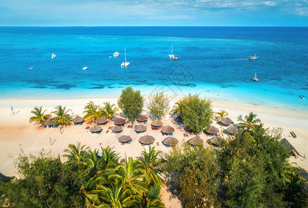 阳光明媚的日子里,印度洋的沙滩上俯瞰雨伞棕榈树非洲桑给巴尔的暑假热带景观,棕榈树,阳伞,船,游艇,蓝色的水背景图片