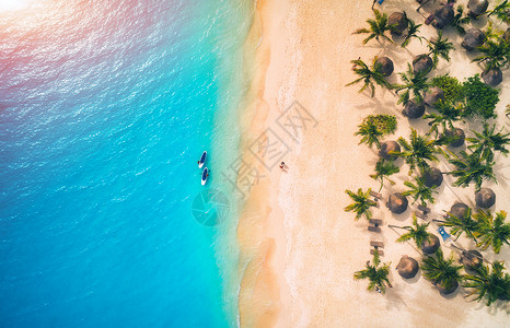 日落时,遮阳伞沙滩上的棕榈树海上的皮艇的鸟瞰图非洲桑给巴尔的暑假热带景观棕榈树,阳伞,船,沙子,碧水的风景背景图片