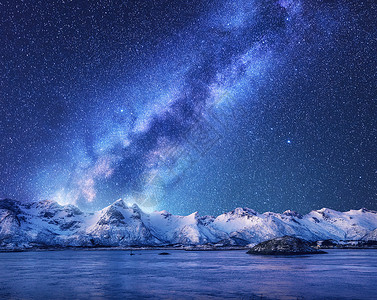 紫色的银河覆盖着挪威冬天的山脉大海风景雪岩,天空星星,倒影水中,峡湾洛芬岛美丽的银河背景图片