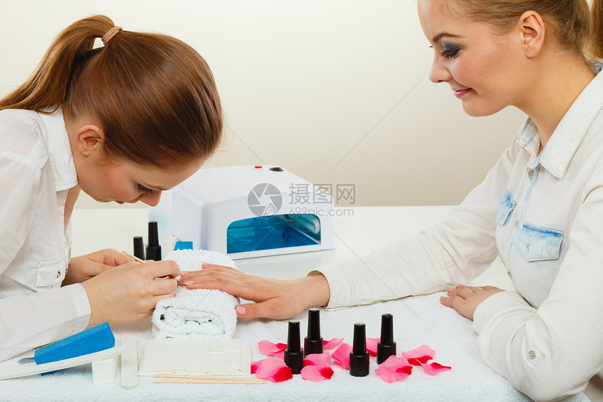 美甲工艺美容院的轻美容师女顾客女客户手握桌上的指甲油,毛巾文件照明仪器专业美甲师绘画女指甲图片