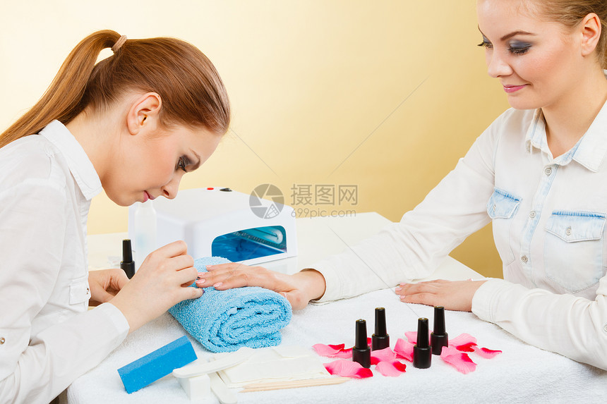 美甲工艺美容院的轻美容师女顾客女客户手握桌上的指甲油,毛巾文件照明仪器专业美甲师绘画女指甲图片