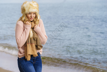 女人穿着温暖时尚的秋装,戴着毛茸茸的大帽子,但感觉很冷女海滩上放松散步时发冷穿着时尚服装的女海边感觉很冷背景图片