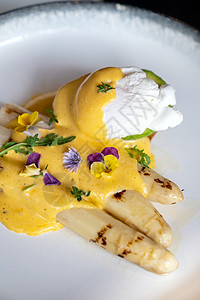 帕尔马干酪美味的烤白芦笋与煮鸡蛋与荷兰风味酱装饰与食用五颜六色的花背景