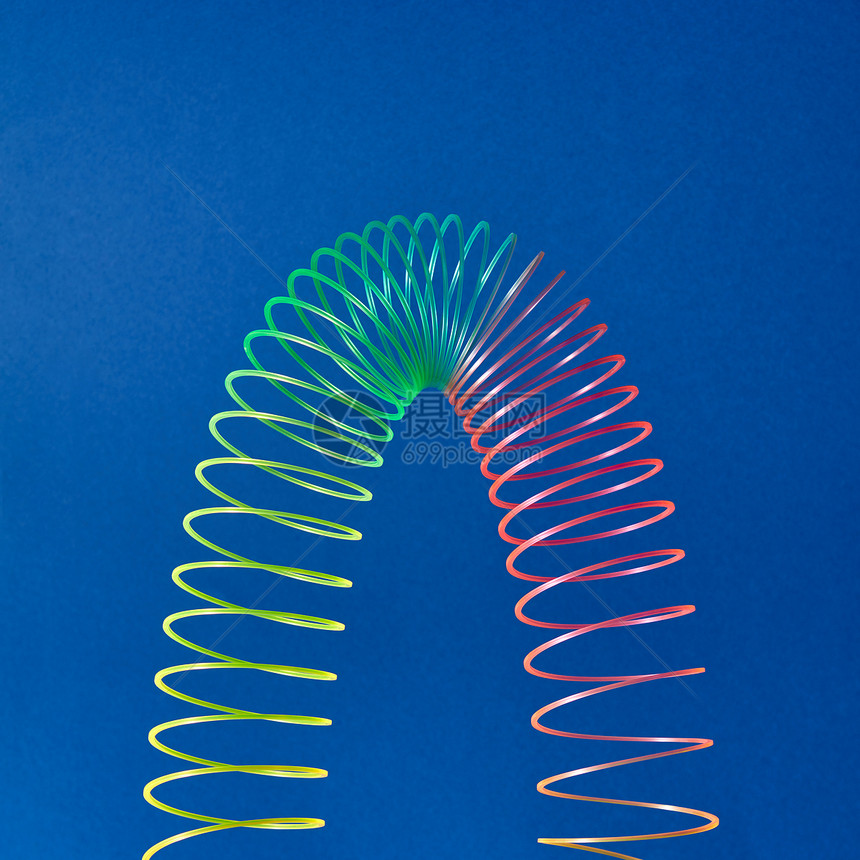 蓝色背景上以抛物线的形状蓝色背景上编彩色玩具螺旋蓝色背景上的柔塑料彩虹弹簧图片