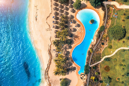 鸟瞰游泳池,雨伞,沙滩,绿树蓝海夏季日落时印度洋海岸的风景景观与蔚蓝的水,阳伞,棕榈树豪华度假村自然背景图片